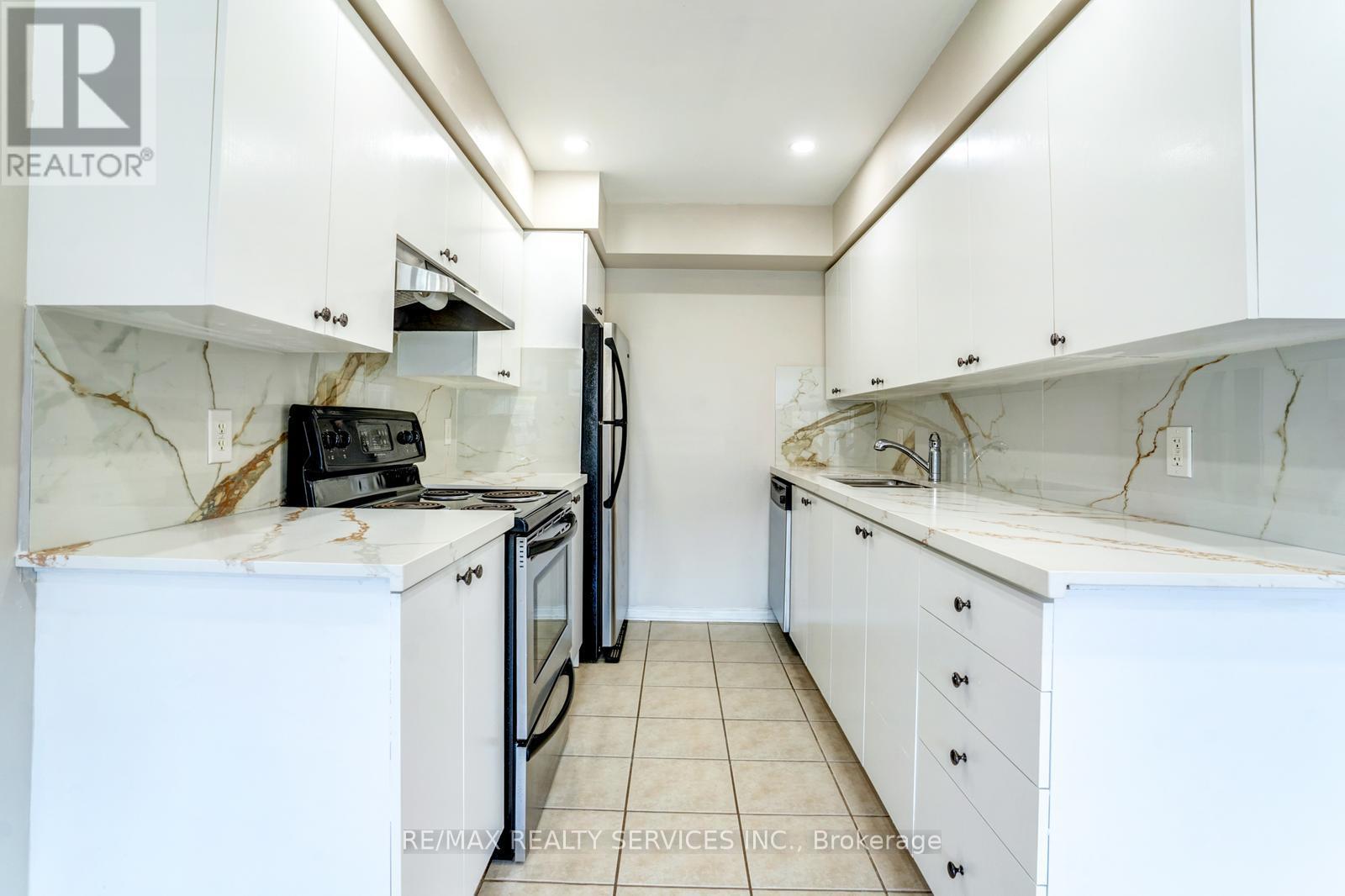 A white kitchen with a marble counter top and a refrigerator.