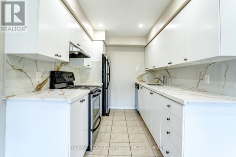 A white kitchen with a marble counter top and a refrigerator.