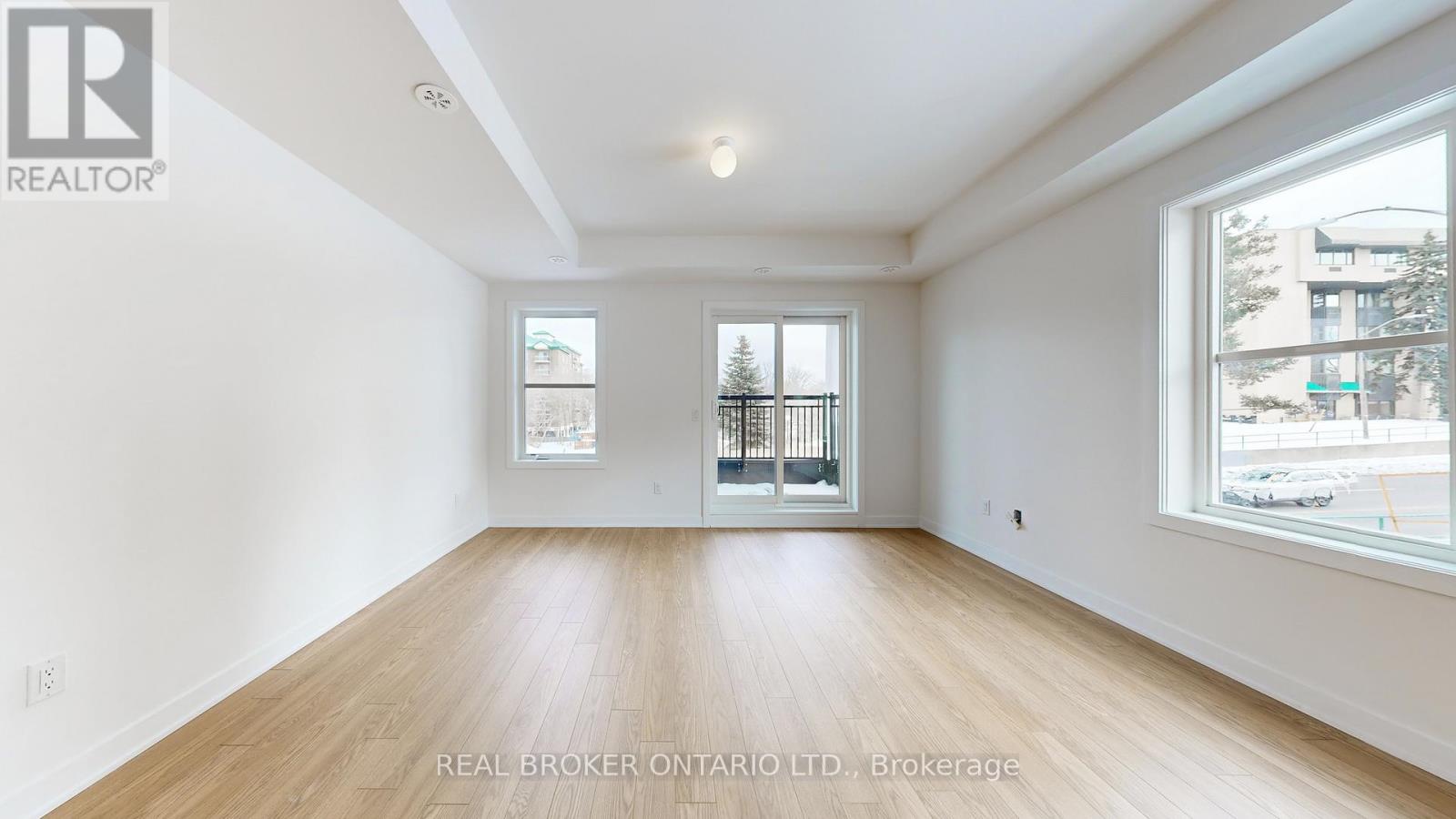 A spacious room with wooden flooring and two windows.