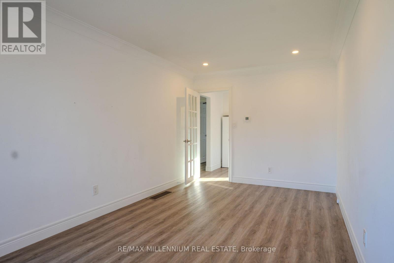 A room with wooden flooring and white walls, with a doorway leading to another room.