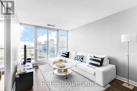A living room with a white couch and a large window overlooking a cityscape.
