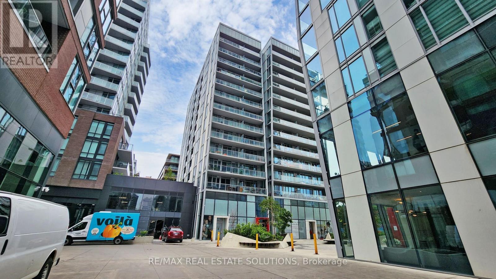 A modern building with a glass facade is surrounded by other buildings.