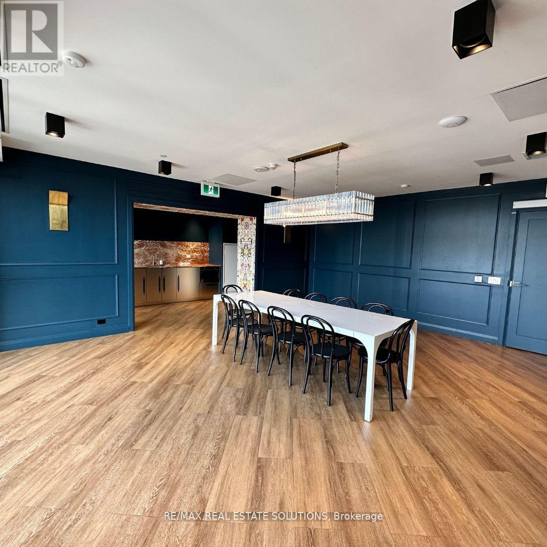 A room with a long table and chairs in the foreground and a kitchen area in the background.