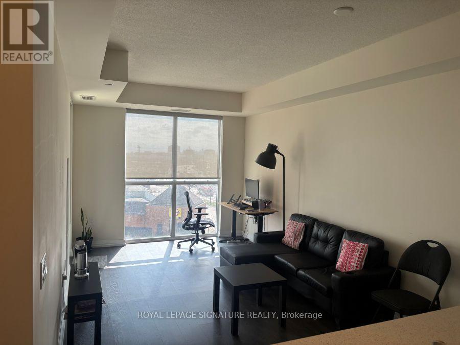 A living room with a black couch and a desk with a lamp.