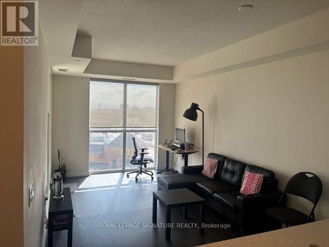 A living room with a black couch and a desk with a lamp.