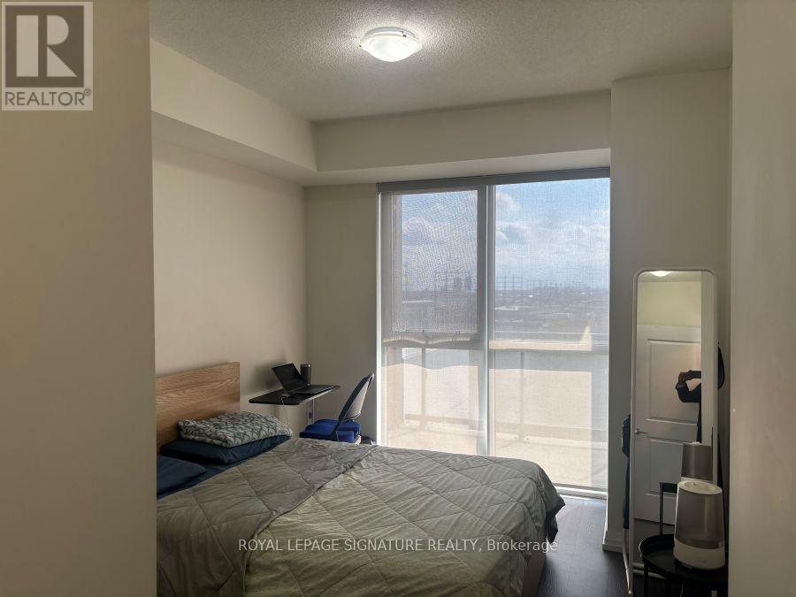 A bedroom with a bed, nightstand, and a window with a view of a fence and trees.