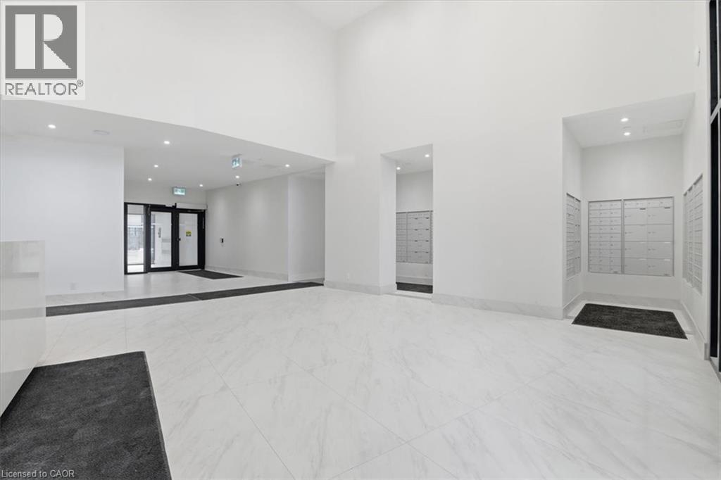 A spacious, white-walled room with a black carpet and a realtor logo on the wall.