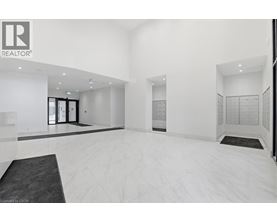 A spacious, white-walled room with a black carpet and a realtor logo on the wall.