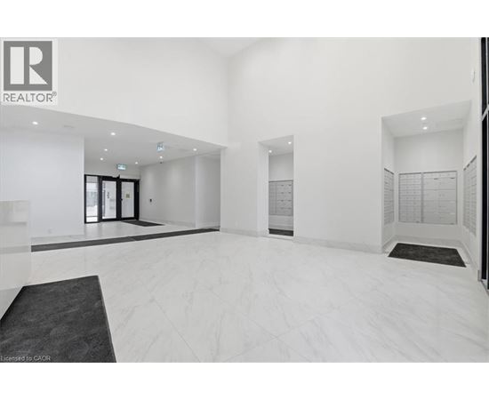 A spacious, white-walled room with a black carpet and a realtor logo on the wall.