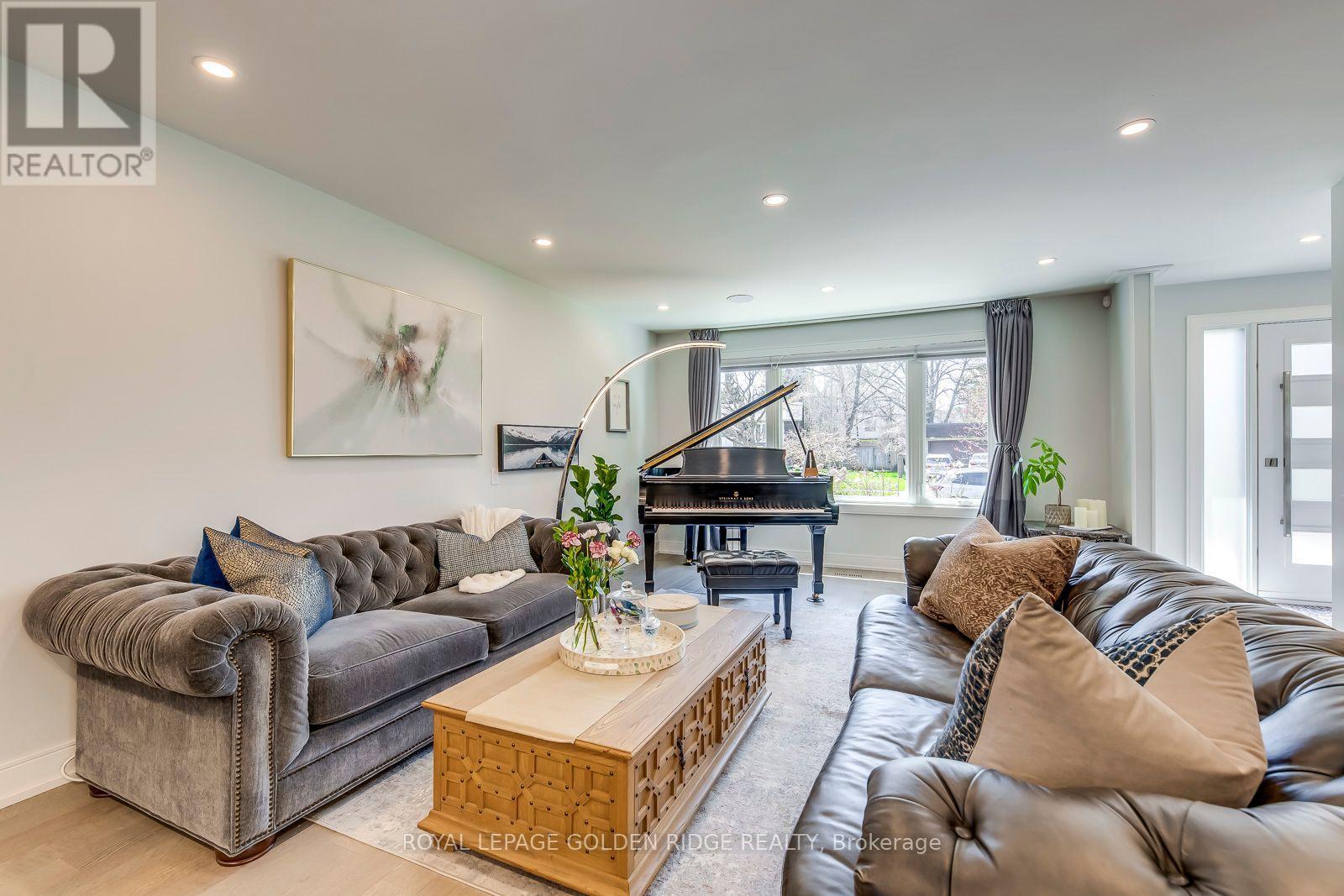 A living room with a grey couch, a brown leather couch, a wooden coffee table, and a piano.