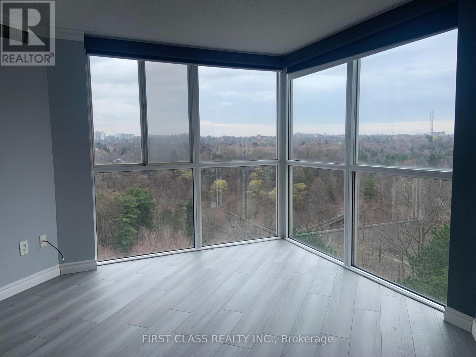 A room with a view of trees and a cloudy sky through large windows.