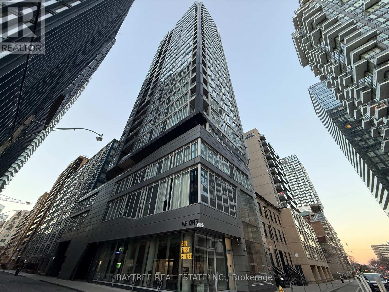 A tall building with the words "Baytree Real Estate, Inc." on its facade is surrounded by other skyscrapers.