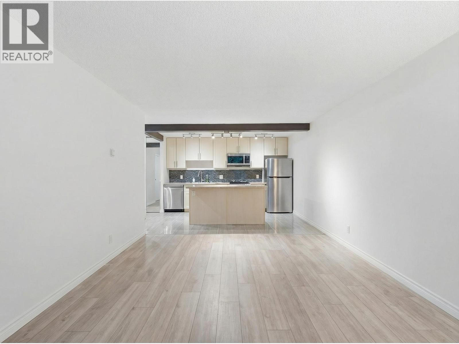 A spacious kitchen with a wooden floor and white walls.