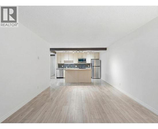 A spacious kitchen with a wooden floor and white walls.