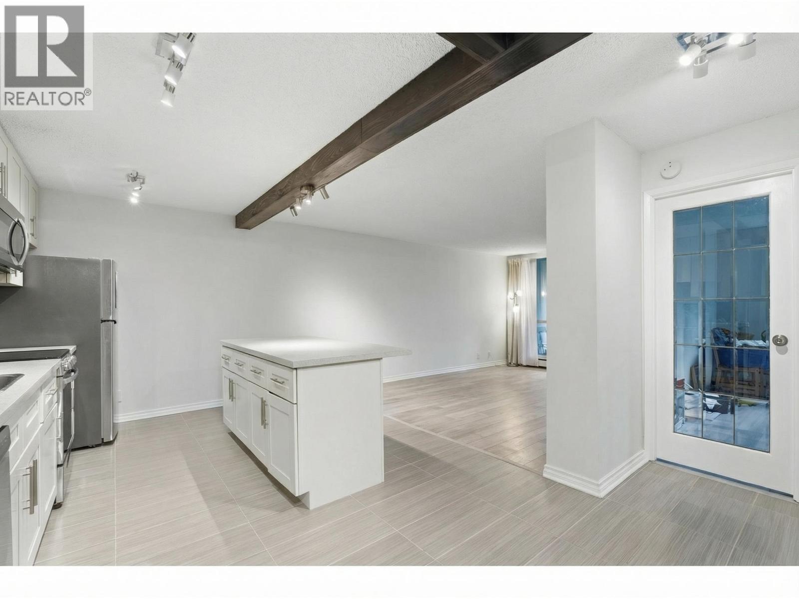 A spacious kitchen with white cabinets and a wooden ceiling beam.