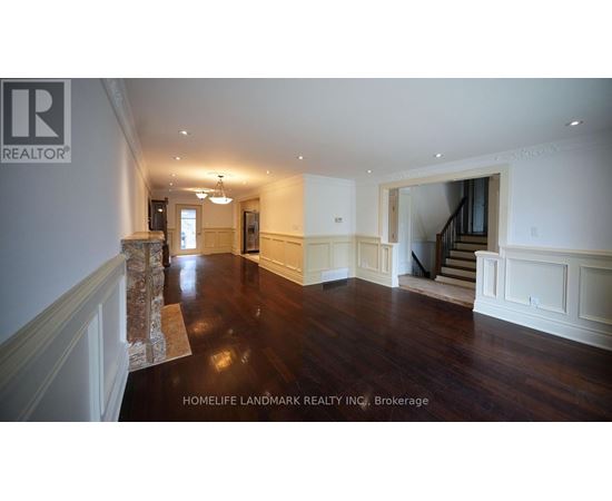 A spacious room with wooden floors and white walls, featuring a staircase and a chandelier.