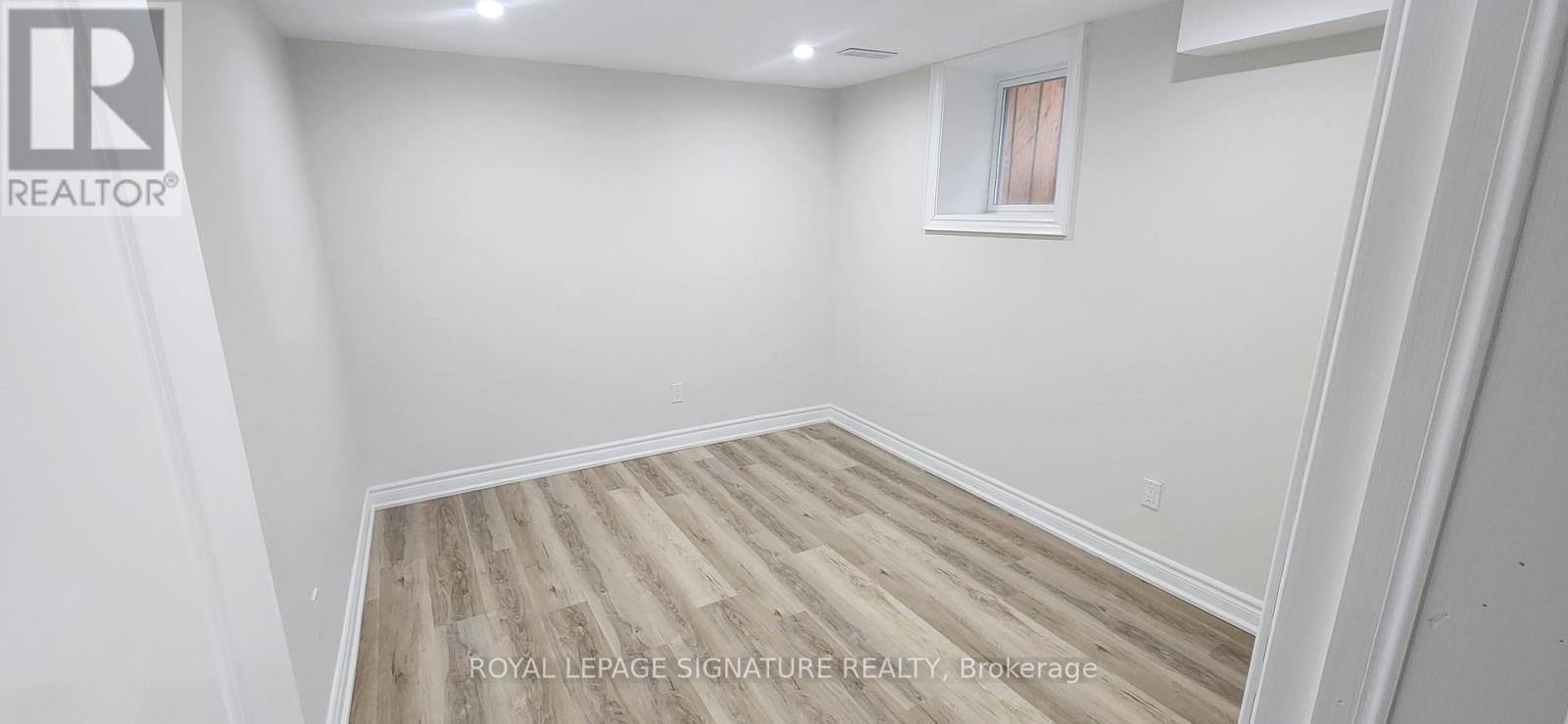 A white room with wooden flooring and a window.