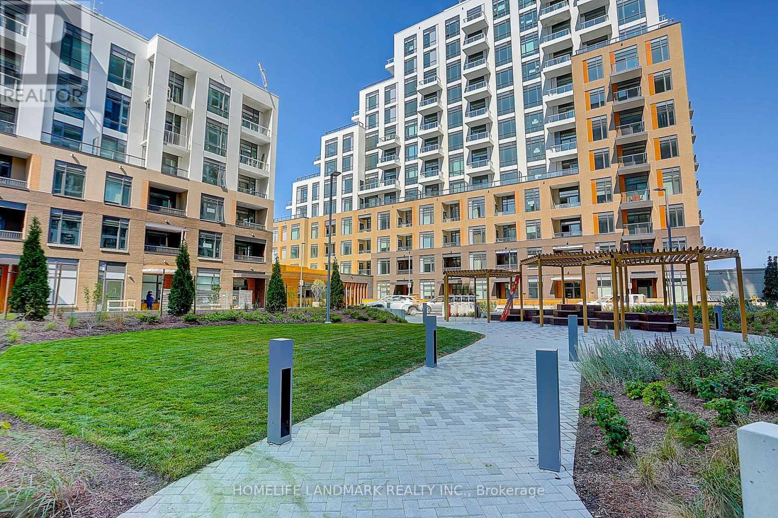 A walkway with a series of posts on it leads through a grassy area between two buildings.
