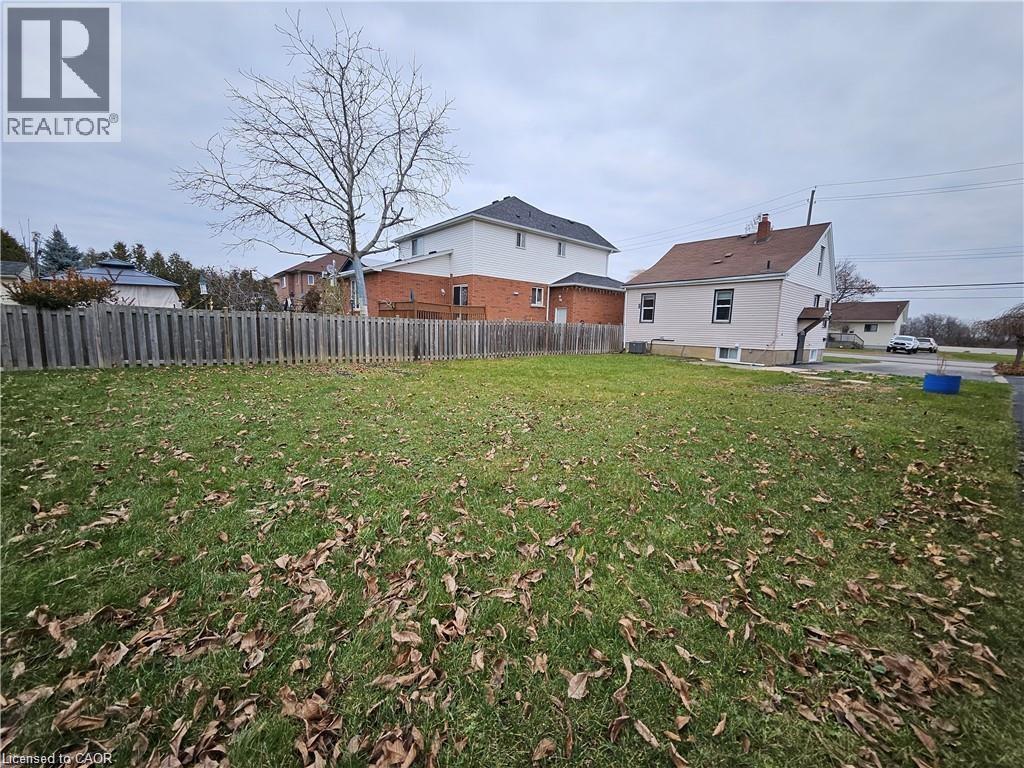 A grassy yard with a fence and two houses in the background.