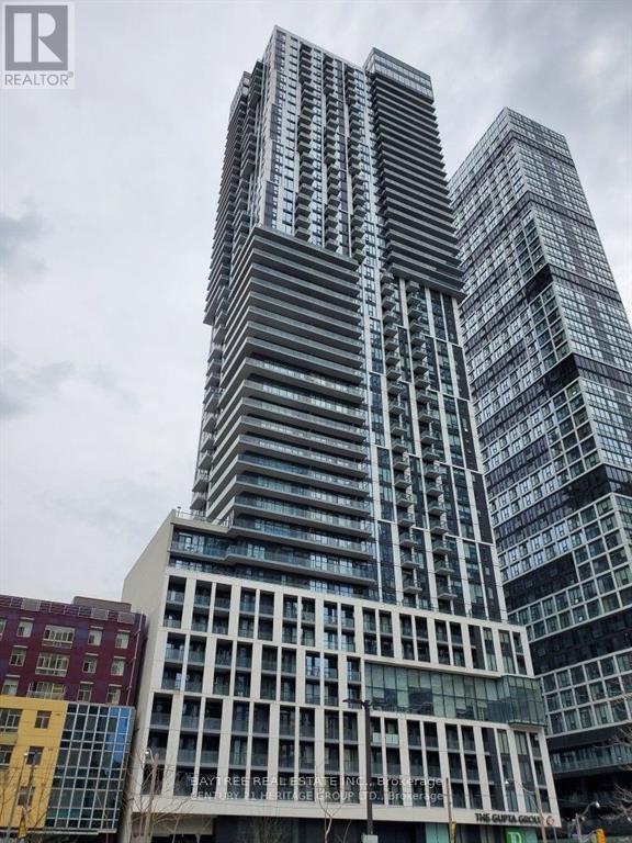A tall building with a glass facade stands in front of other buildings.