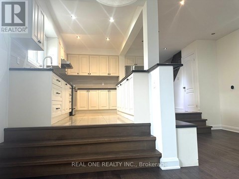 A spacious kitchen with white cabinets and a wooden staircase leading to the upper level.