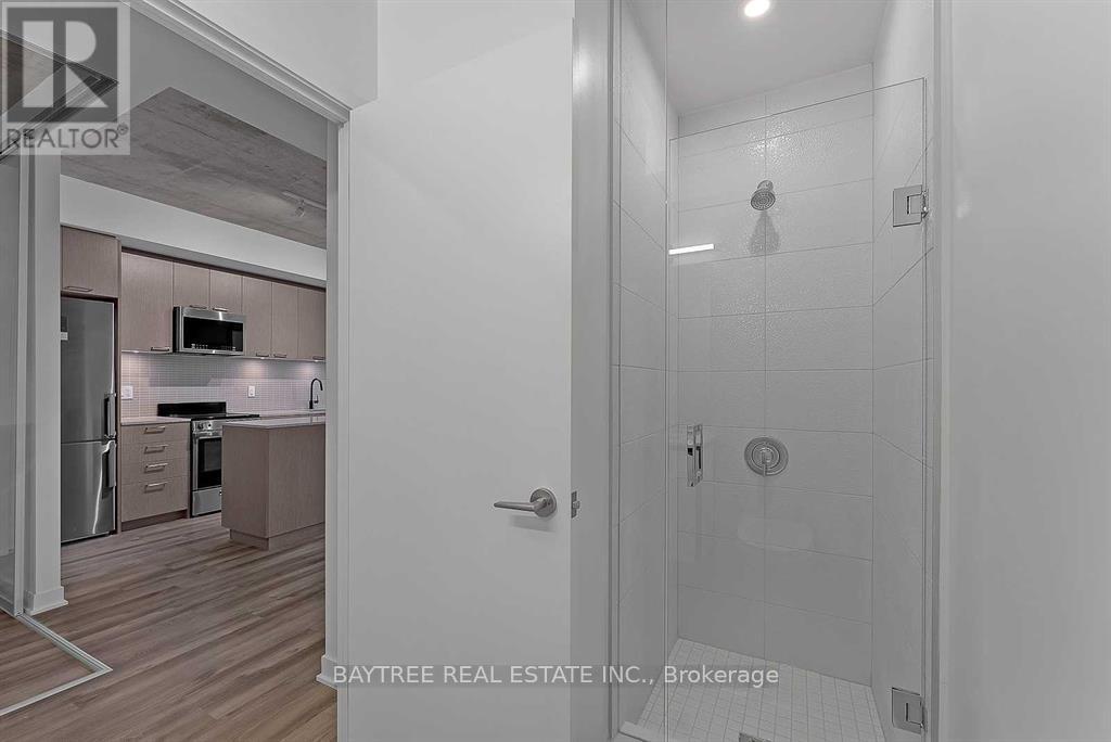 A bathroom with a walk-in shower and a doorway leading to a kitchen.
