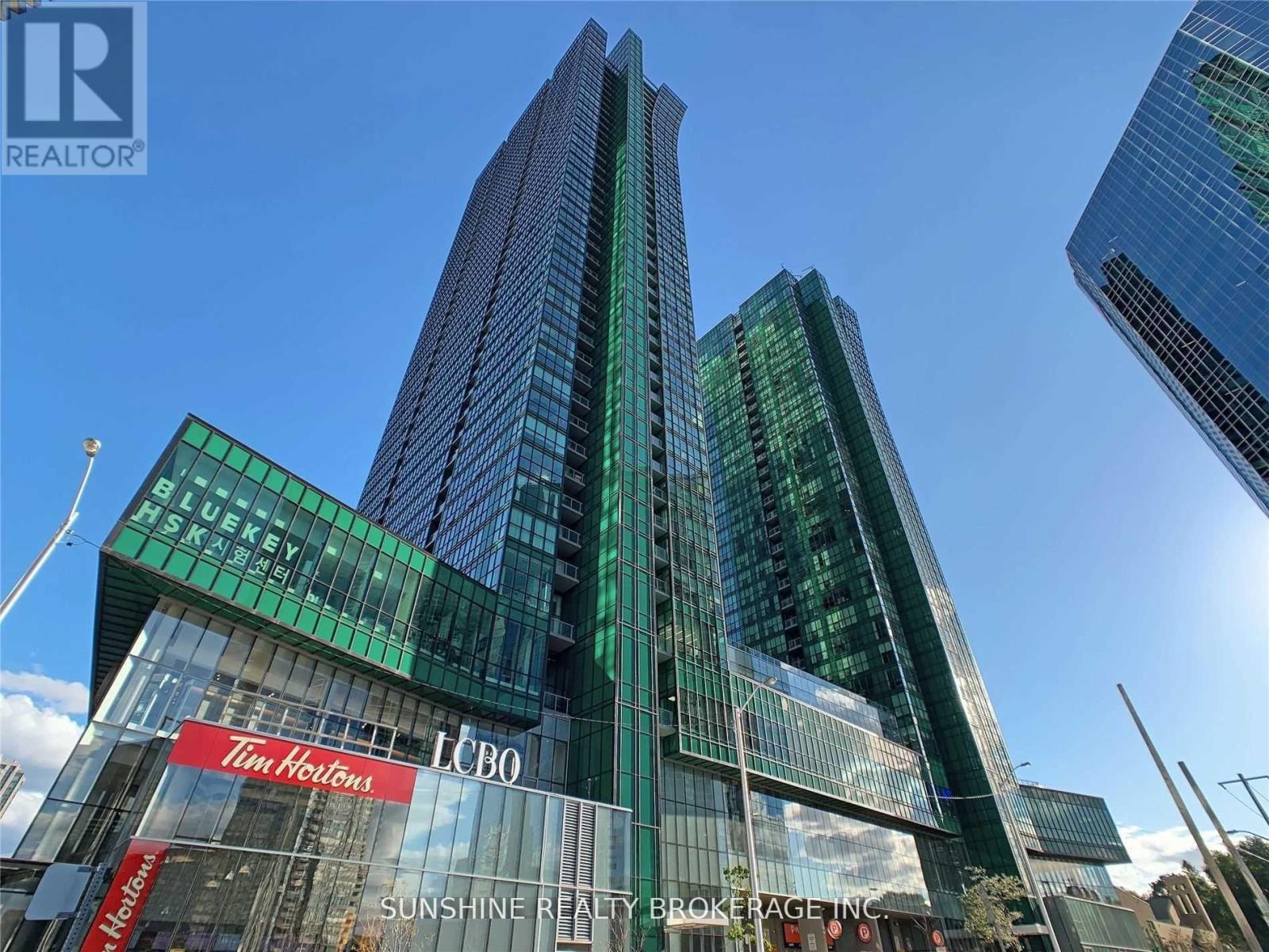 A tall building with a green and blue glass facade and a sign that reads "Sunshine Realty Brokerage Inc.".