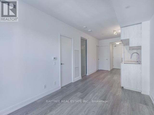 A real estate listing image of a white room with wood flooring and a staircase.