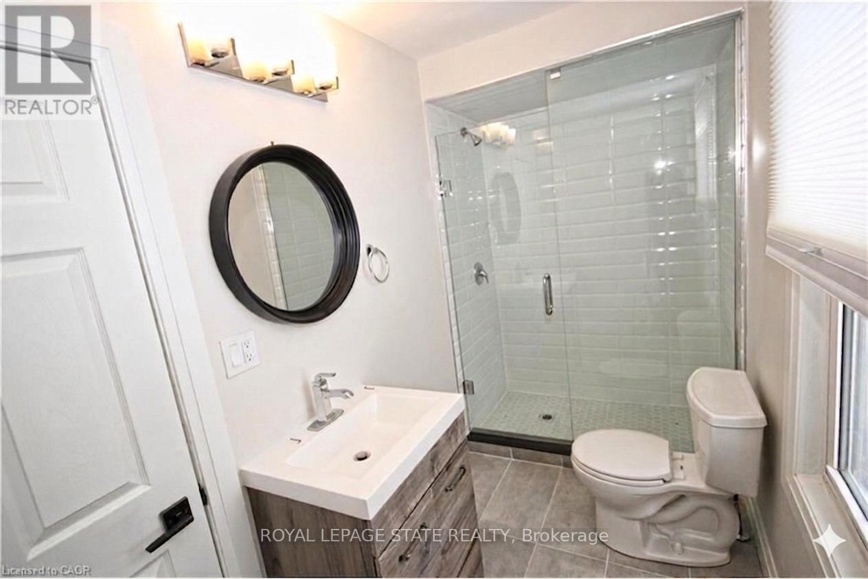 A bathroom with a toilet, sink, mirror and shower.