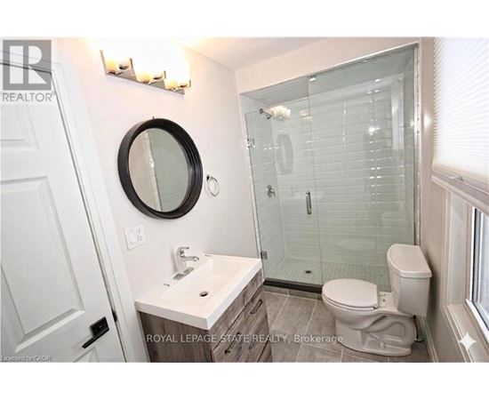 A bathroom with a toilet, sink, mirror and shower.