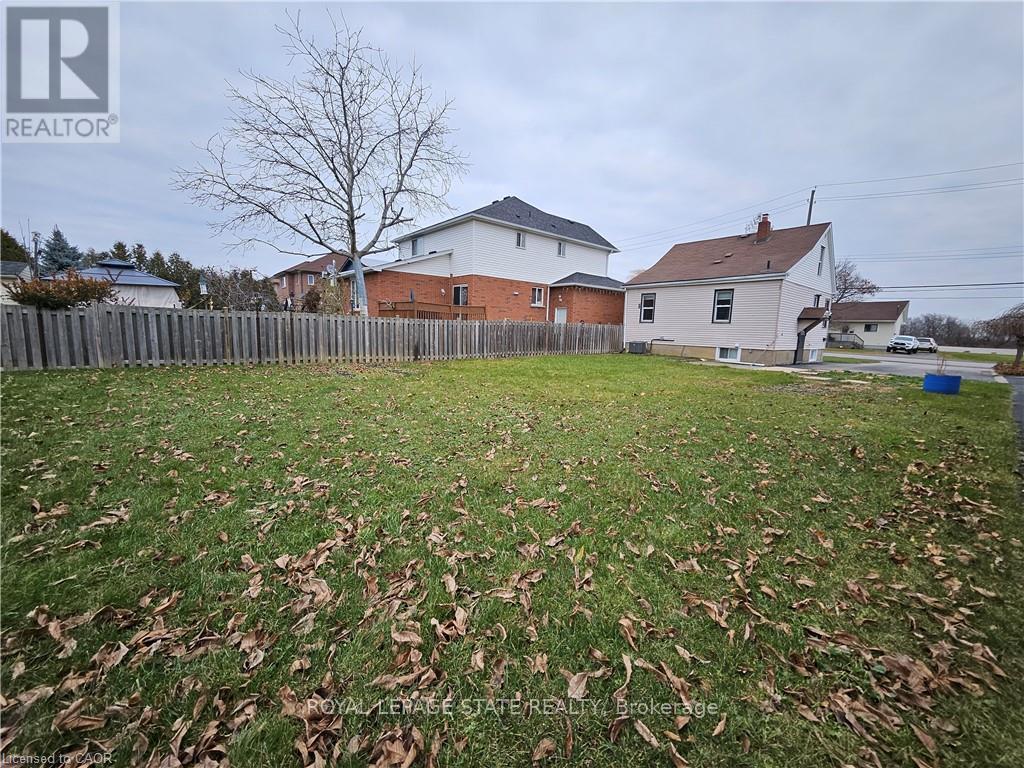 A grassy yard with a fence and two houses in the background.