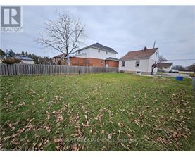 A grassy yard with a fence and two houses in the background.