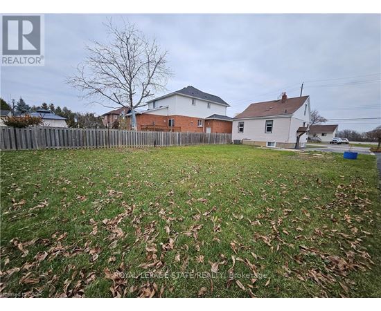 A grassy yard with a fence and two houses in the background.