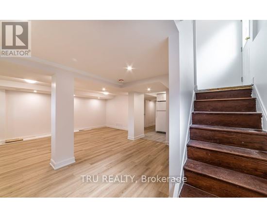 A spacious room with wooden floors and a staircase leading to another level.