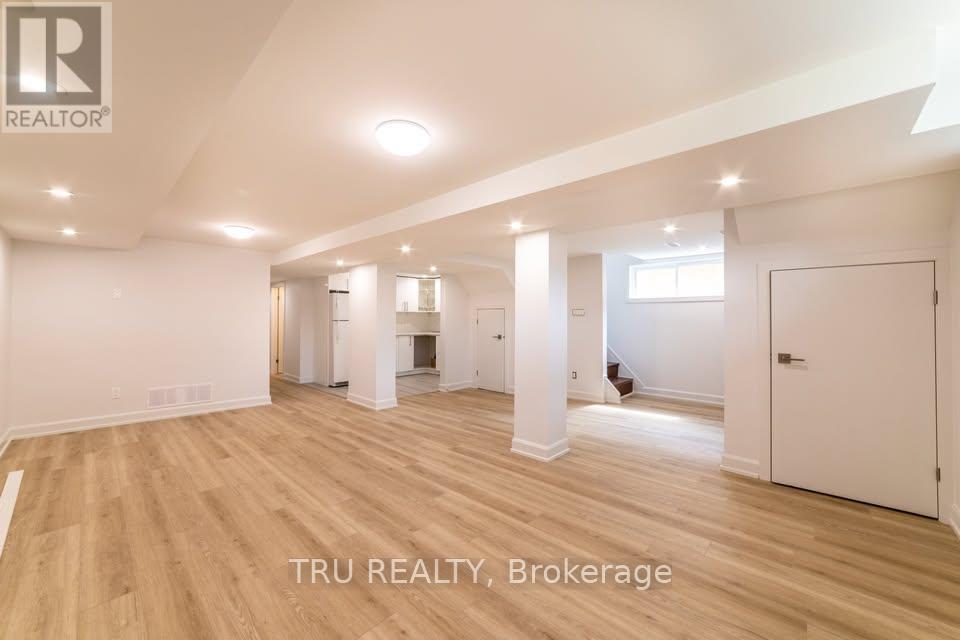 A spacious room with wooden flooring and white walls, with a logo that reads "TRU REALTY, Brokerage" in the bottom right corner.