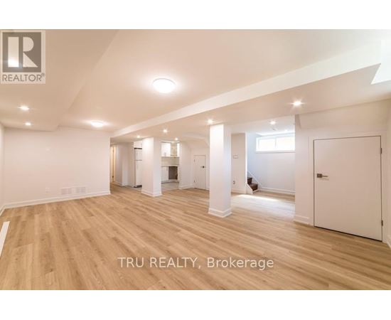 A spacious room with wooden flooring and white walls, with a logo that reads "TRU REALTY, Brokerage" in the bottom right corner.