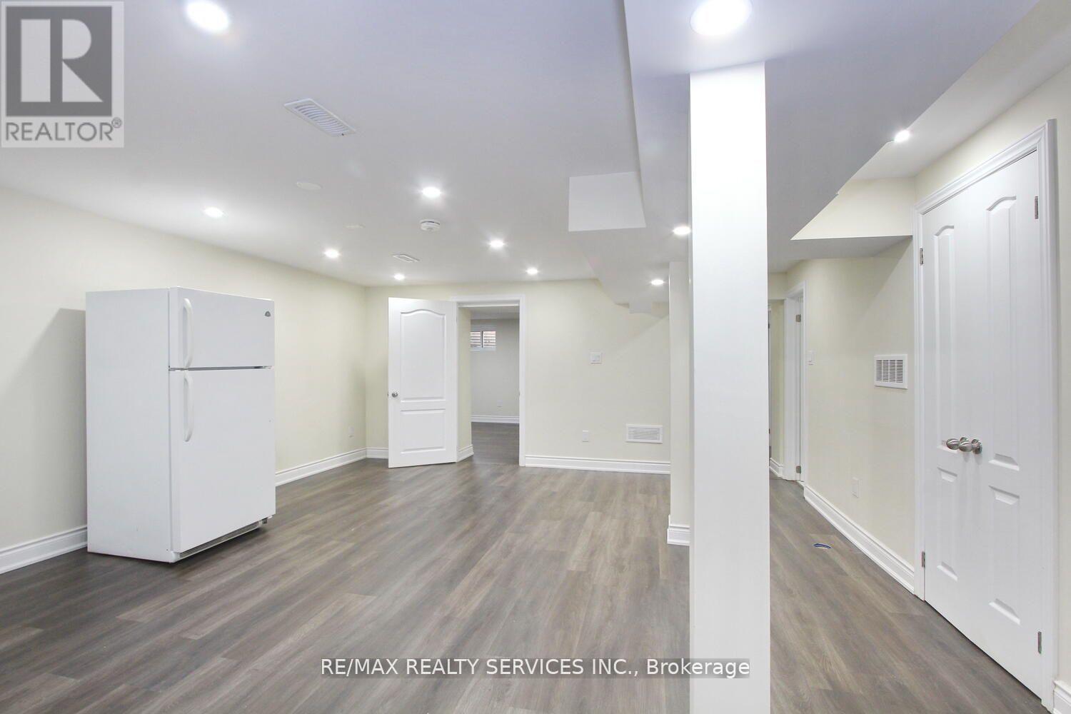A white refrigerator is in a room with wood floors and white walls.