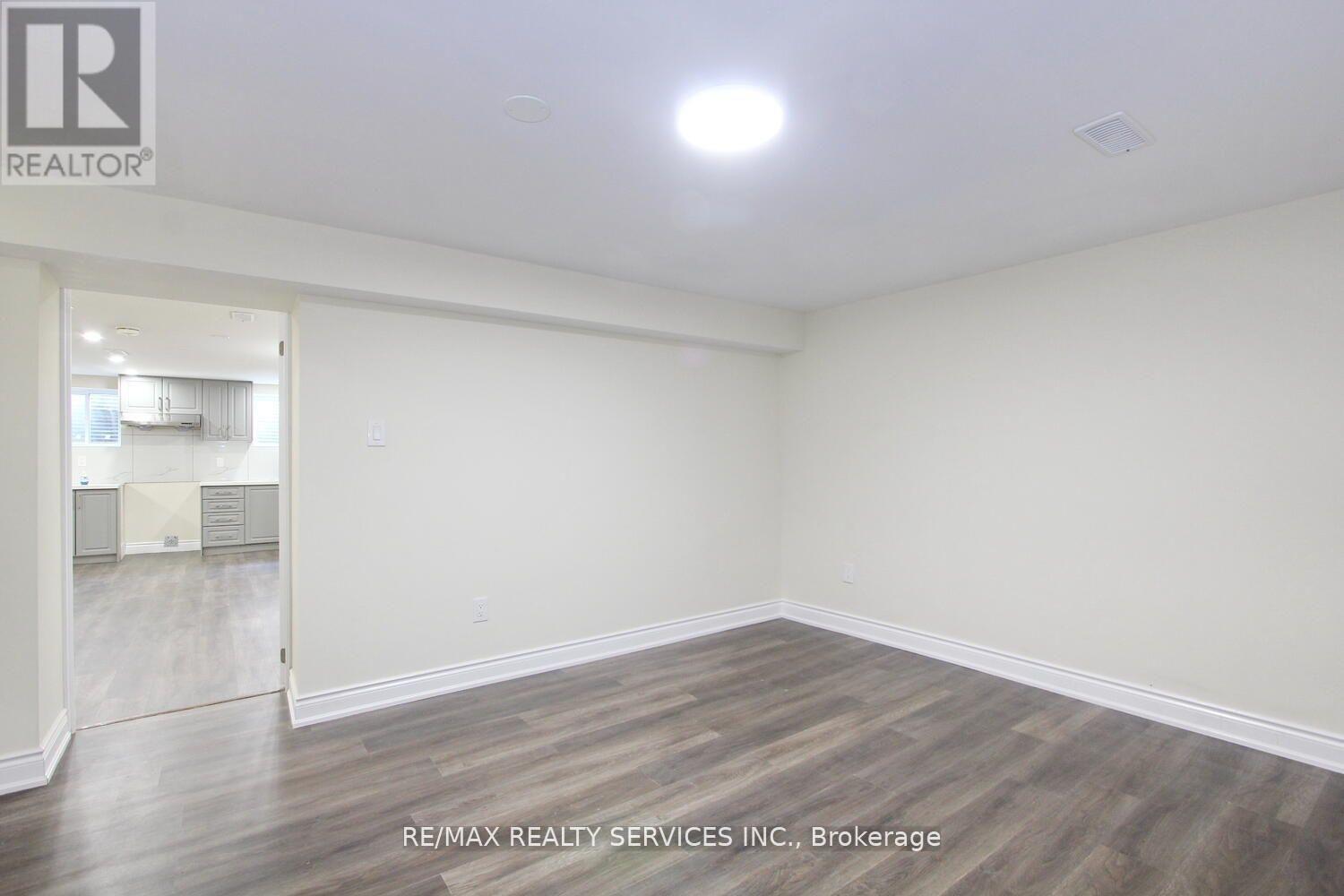 A spacious room with wooden flooring and white walls, with a doorway leading to another room visible in the background.