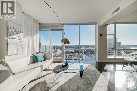 A living room with a white couch and a large window overlooking a cityscape.