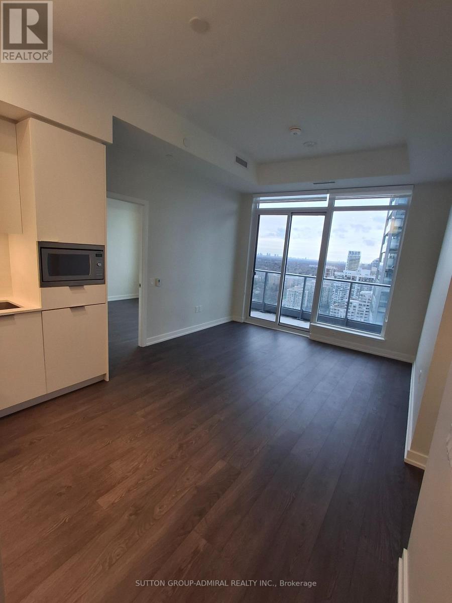 A spacious room with wood flooring and a view of the city through large windows.
