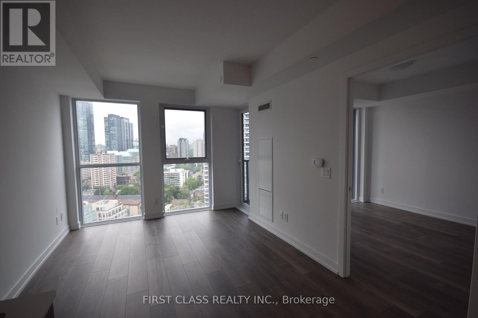 A spacious room with wooden floors and large windows overlooking a cityscape.