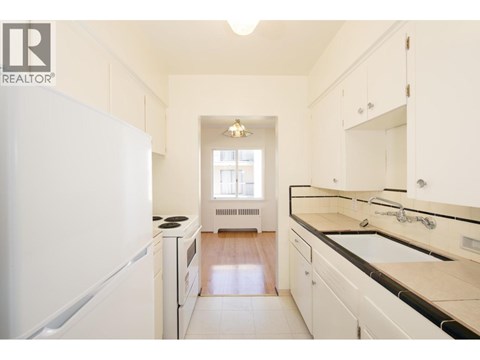A white kitchen with a refrigerator on the left and a sink on the right.