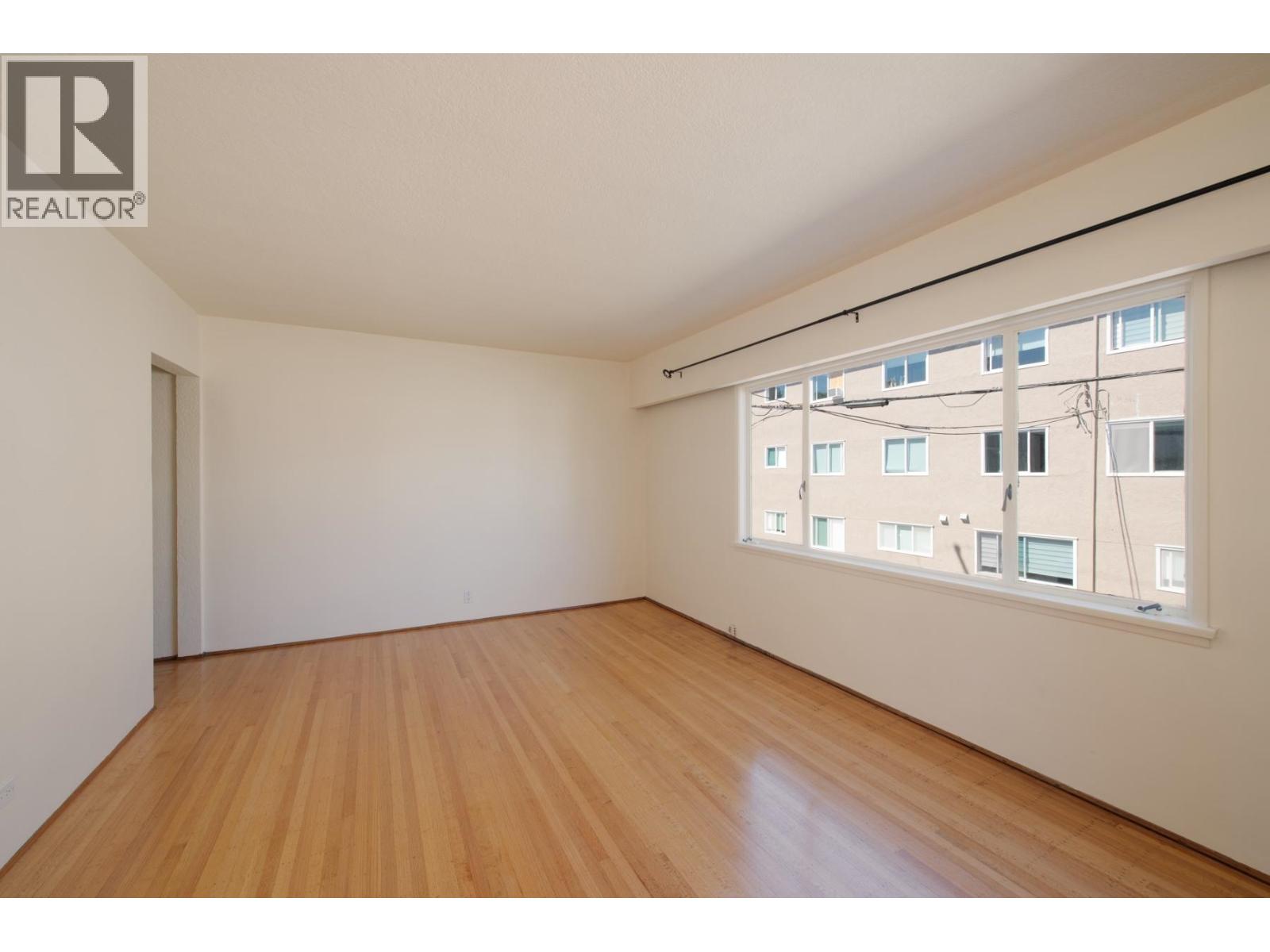 A large empty room with wooden floors and a window overlooking a cityscape.