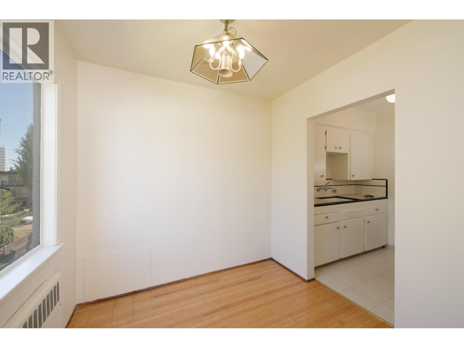 A room with a window and a kitchen area in the background.