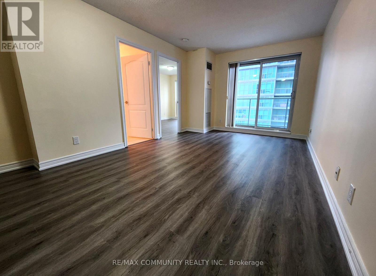 A spacious room with wood flooring and a view of a building outside the window.