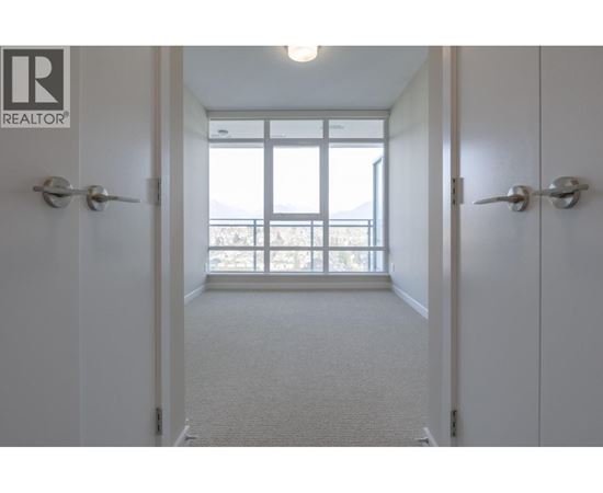 A hallway with a carpeted floor and white walls leading to a door with a window.