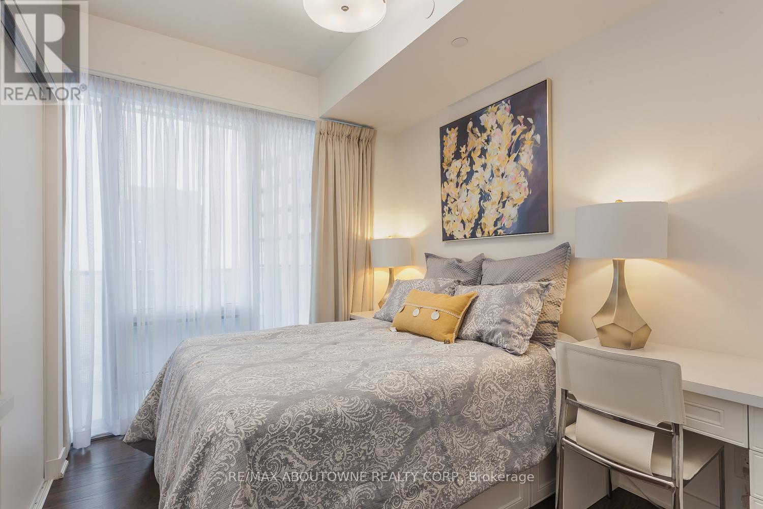 A bedroom with a bed, a desk, and a painting on the wall.