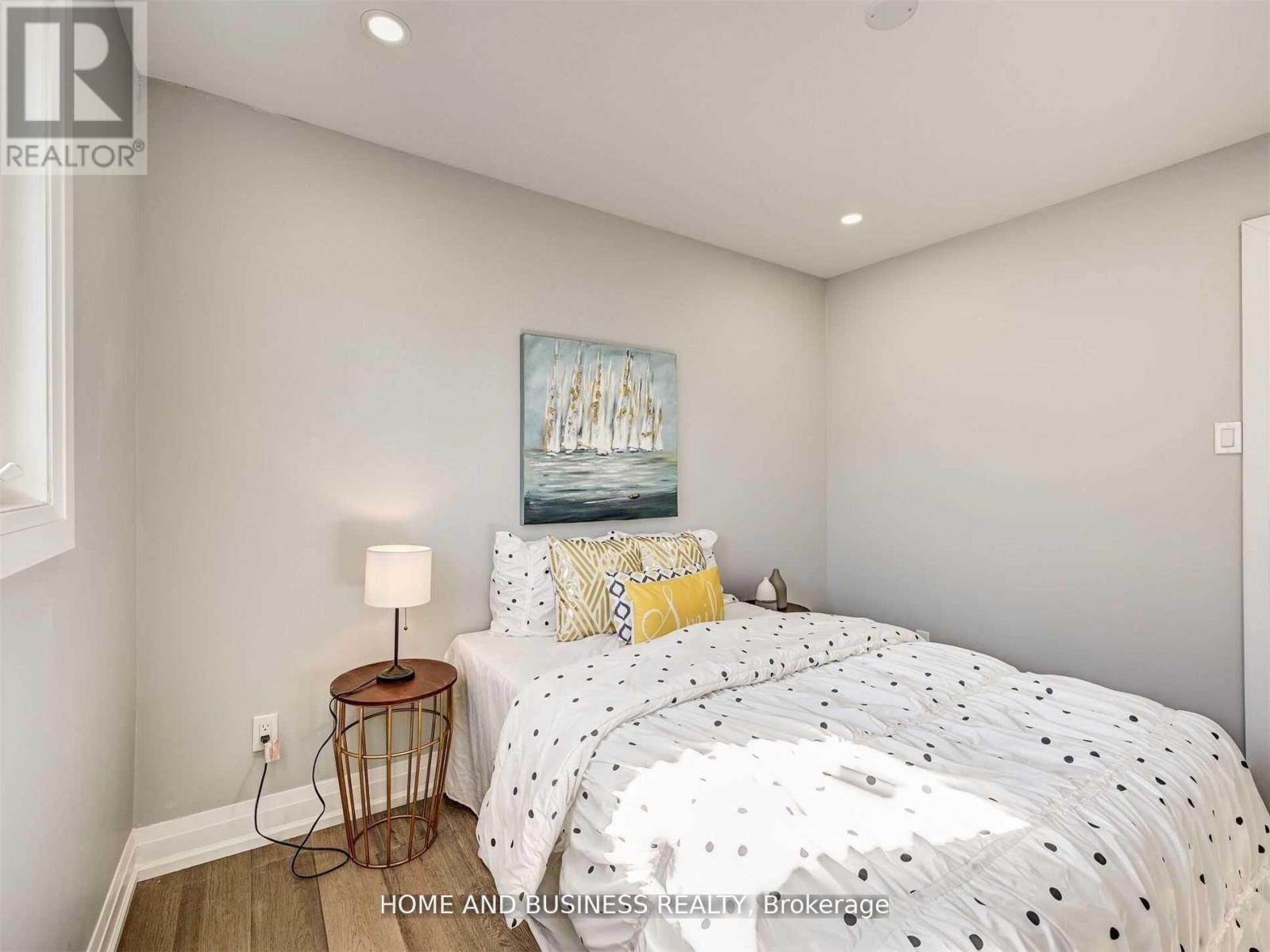 A bedroom with a bed, a nightstand with a lamp, and a painting on the wall.