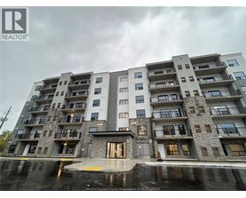 A large apartment building with a grey and white exterior and a puddle in front of it.