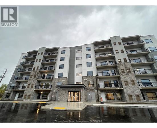 A large apartment building with a grey and white exterior and a puddle in front of it.